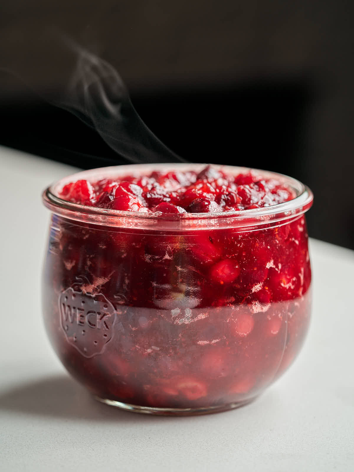 Chunky red cranberry sauce in a small glass jar with steam coming from it.