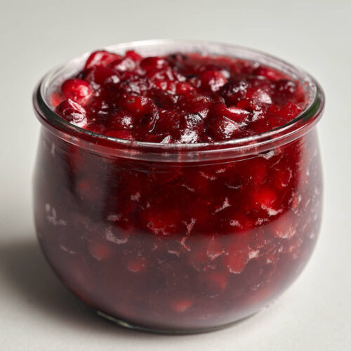 Chunky red cranberry sauce in a small glass jar.