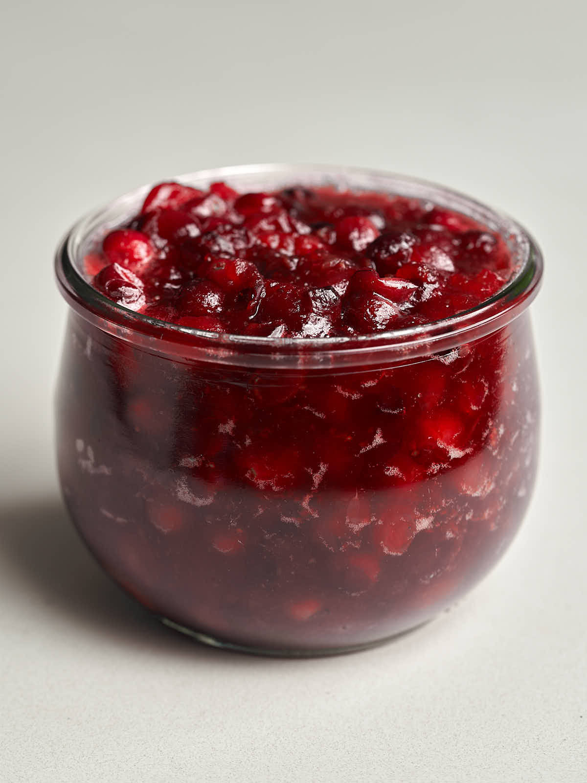 Chunky red cranberry sauce in a small glass jar.