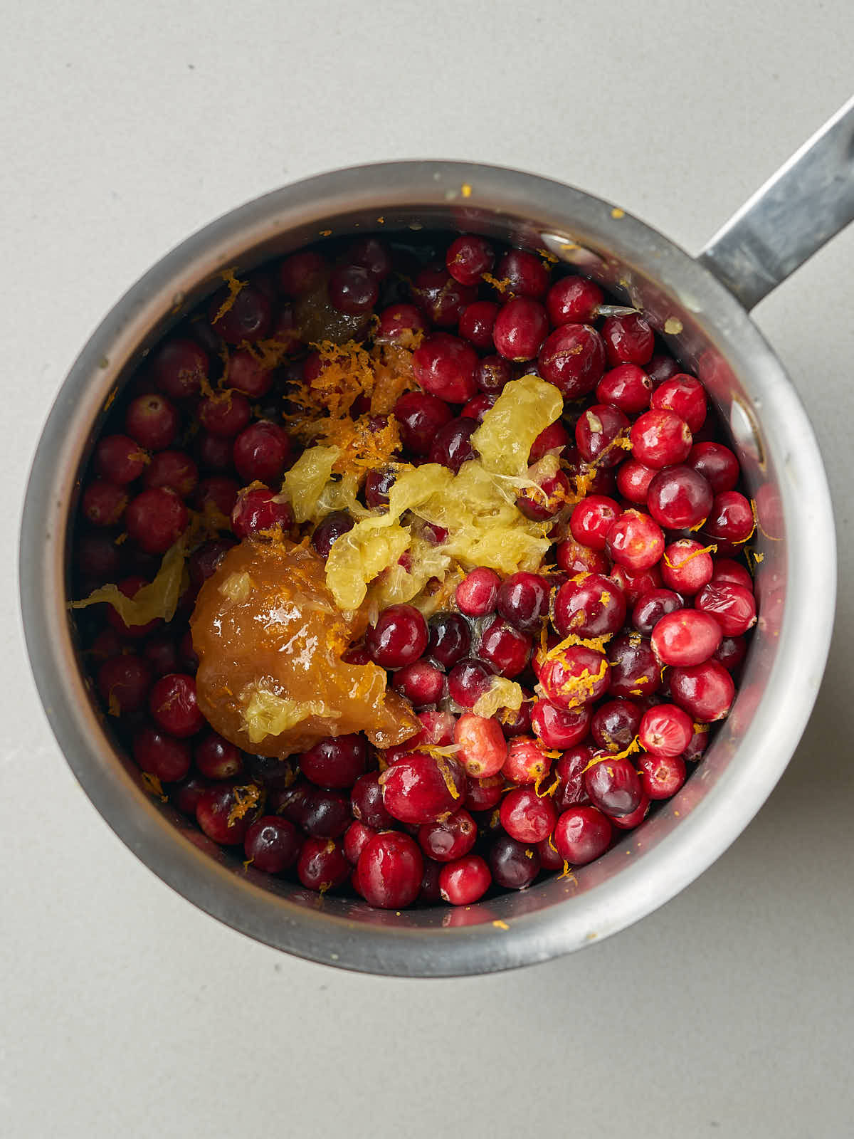 Cranberries, orange zest, and honey in a small silver saucepan.