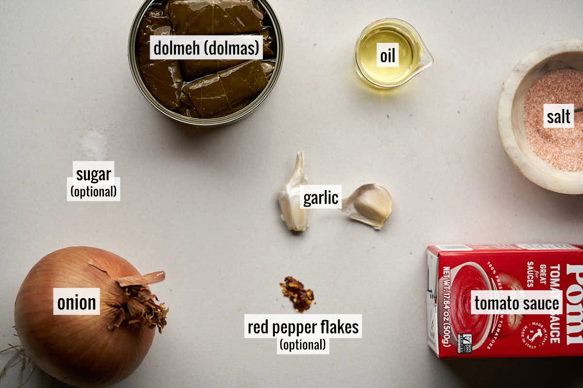 Ingredients to make dolmas in red sauce laid out on a marble countertop.