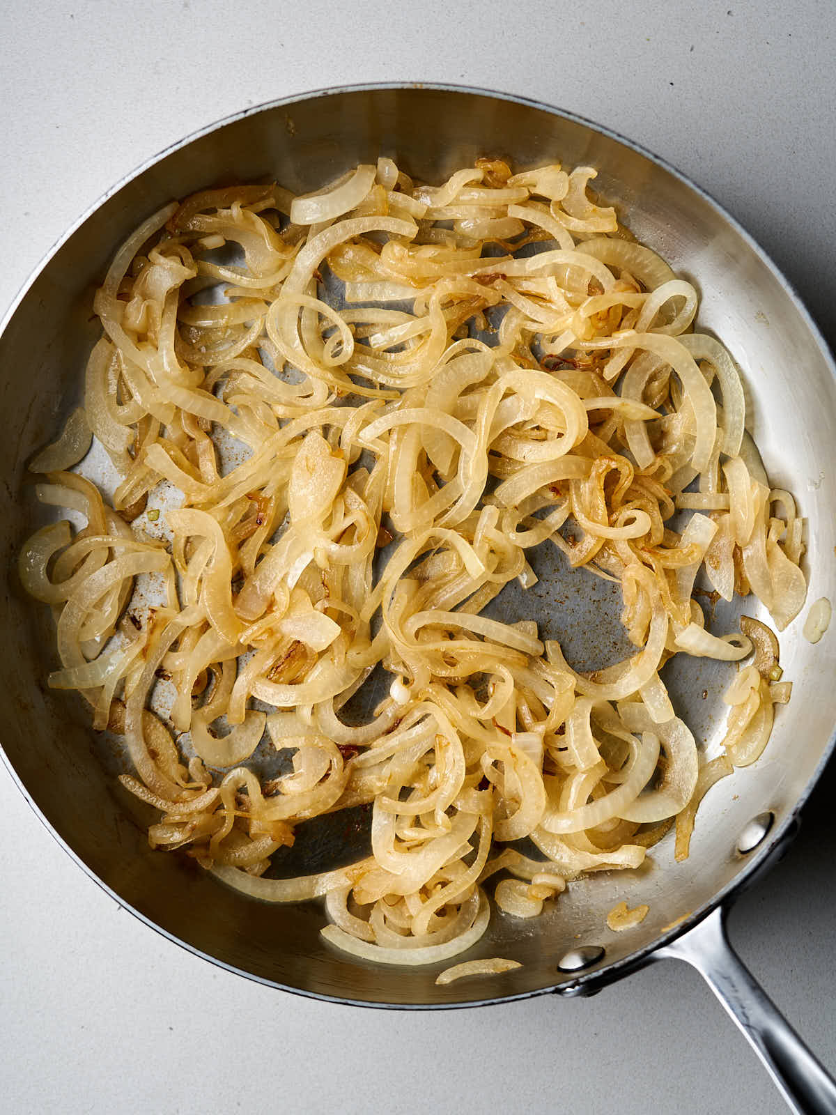 Sliced yellow onions sauteeing in a silver pan.