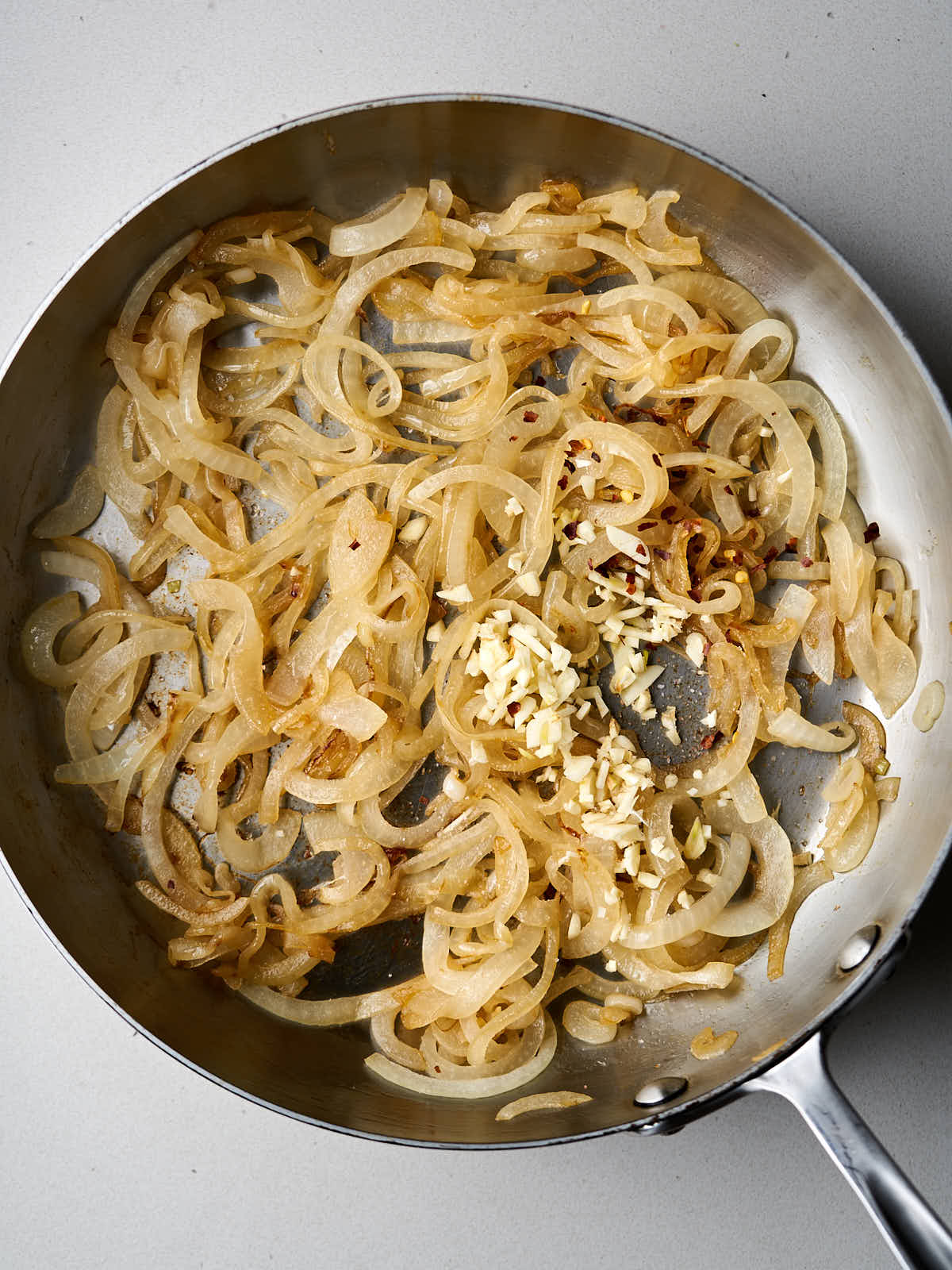 Yellow onions, garlic, and red pepper sauteeing in a pan.