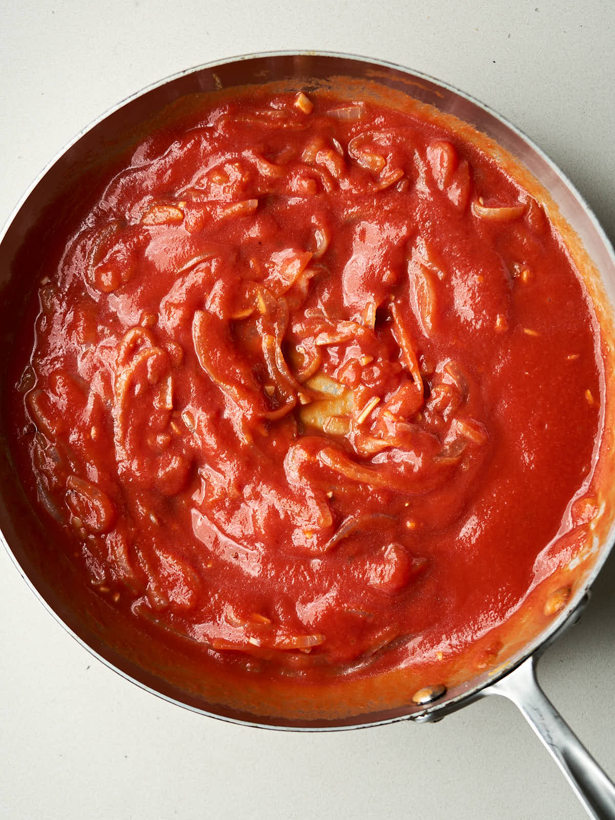 A mix of tomato sauce and onions in a silver pan.