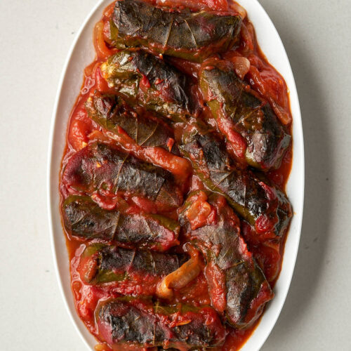 A large oval plate with several baked dolmas in tomato sauce.