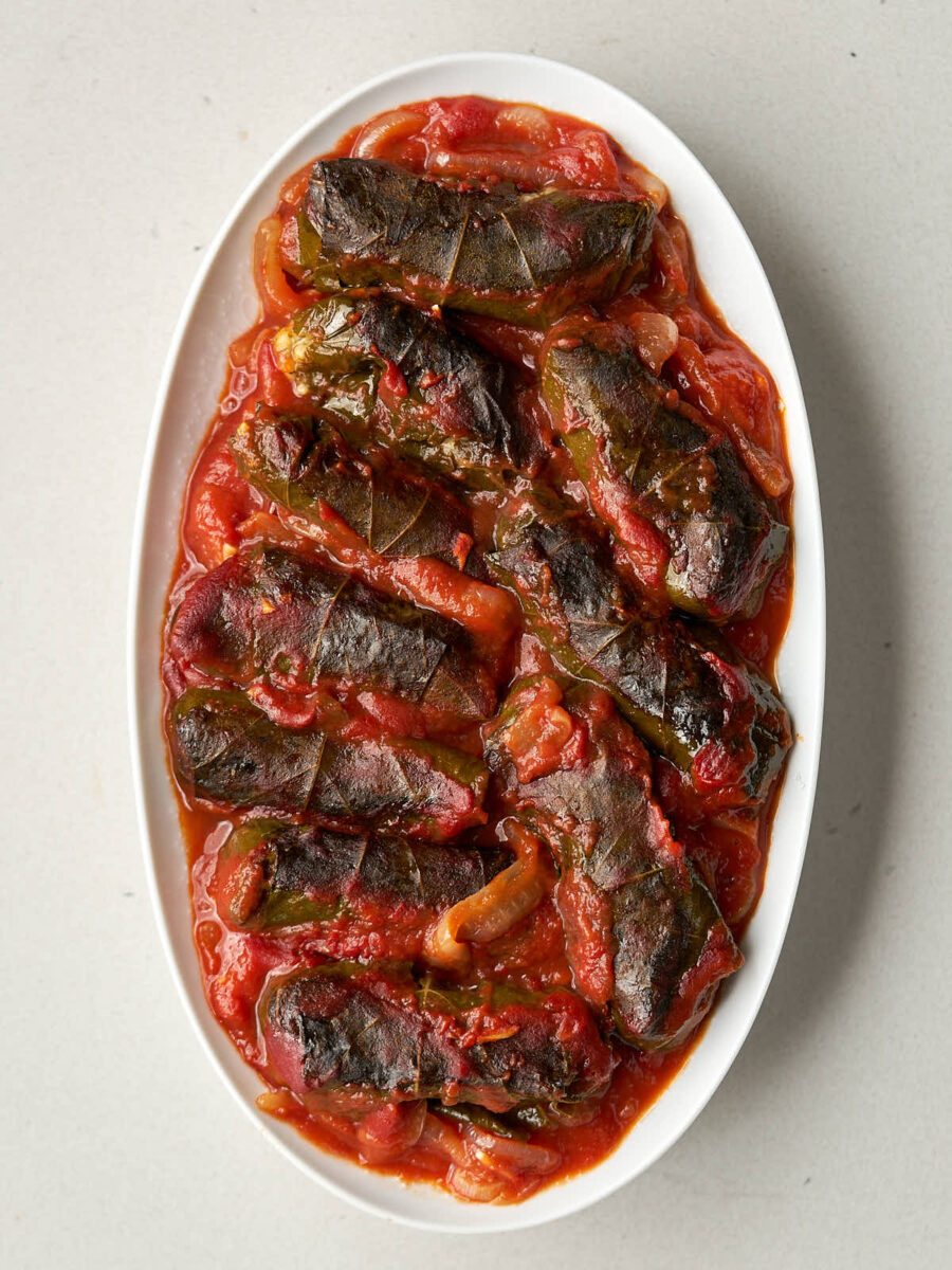 A large oval plate with several baked dolmas in tomato sauce.