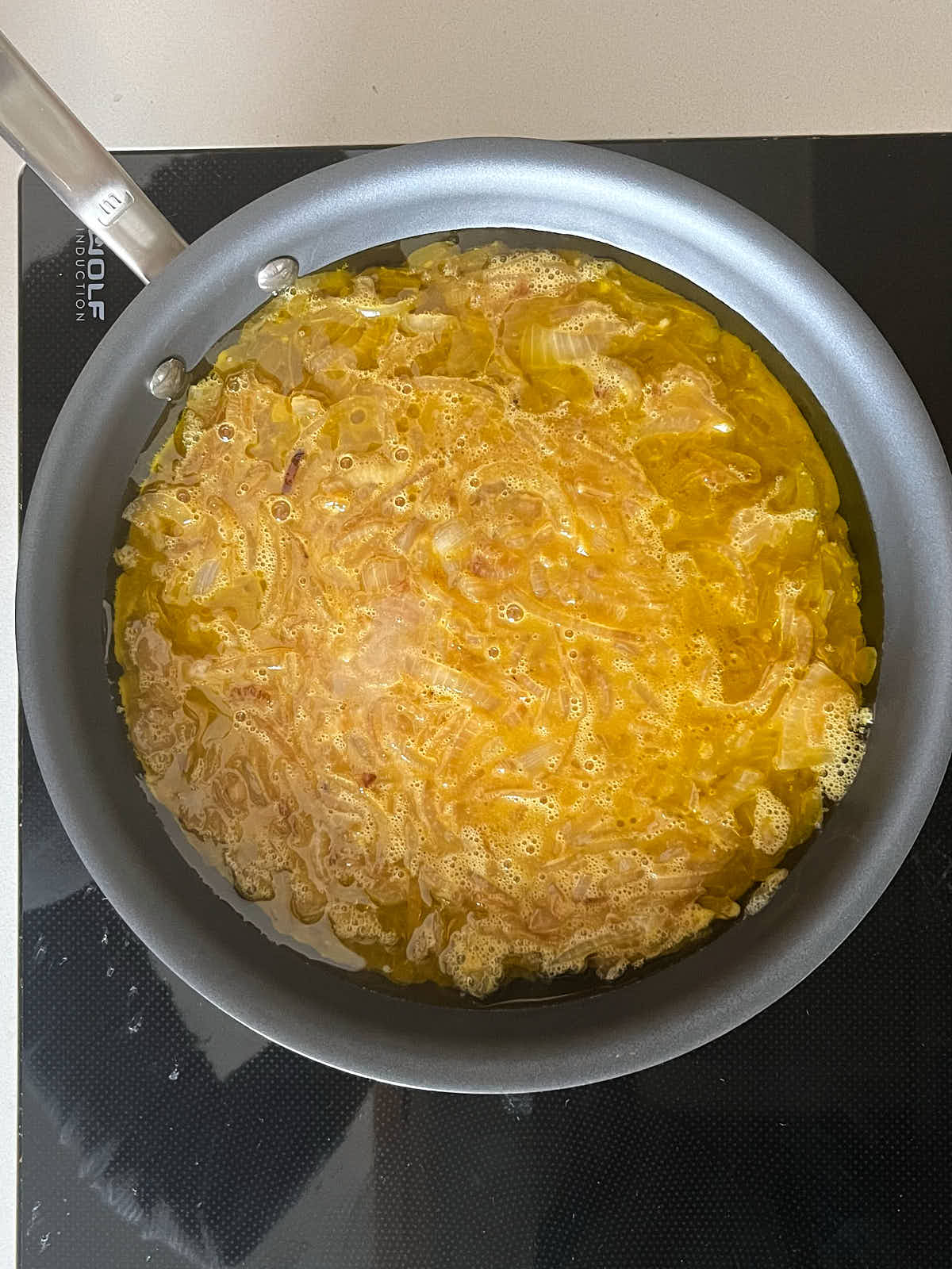 Yellow frittata frying in a non-stick pan.