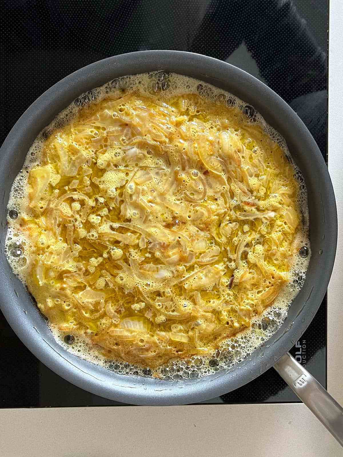 Yellow frittata frying in a non-stick pan.