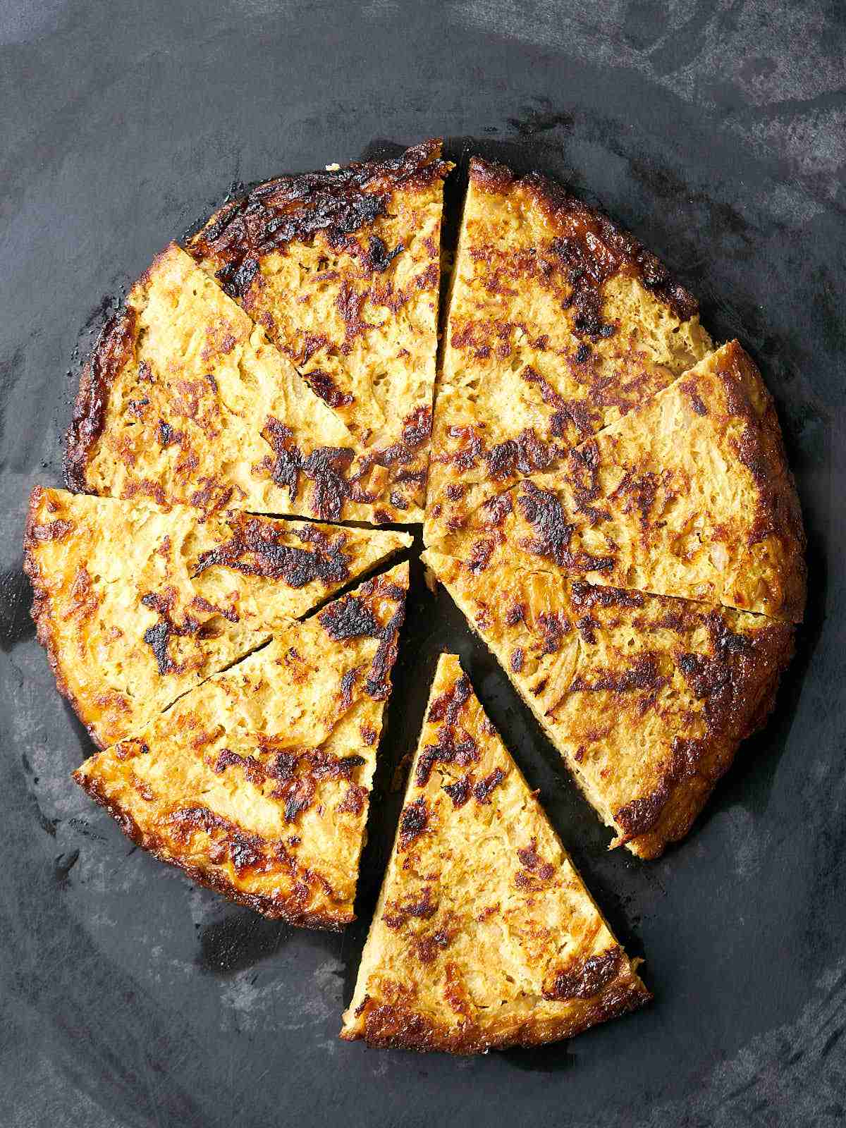 Browned, yellow frittata on a black cutting board, cut into wedges.