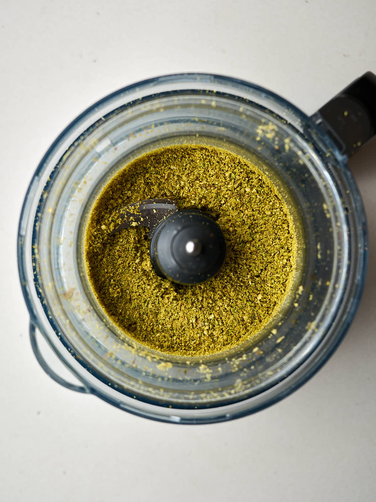 Ground pistachios in the bowl of a food processor.