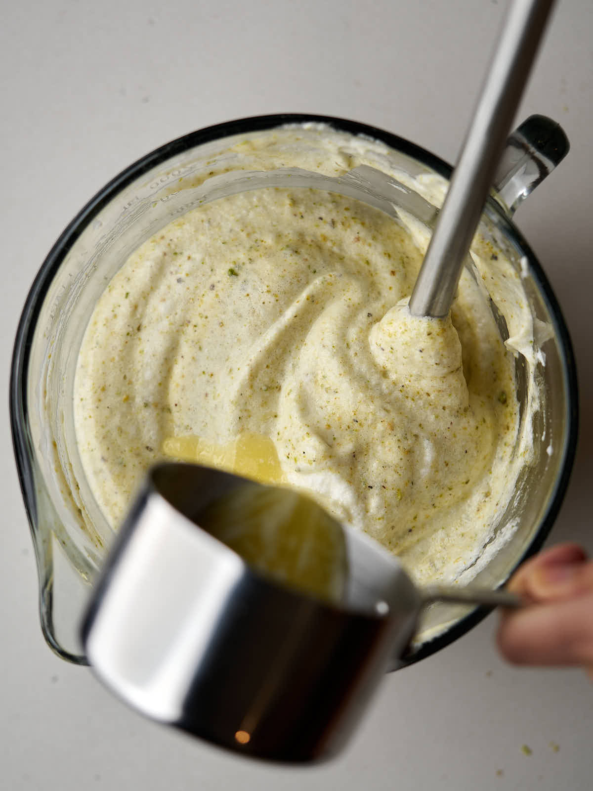 Pouring melted butter from a metal measuring cup into a glass bowl with light green whipped batter.