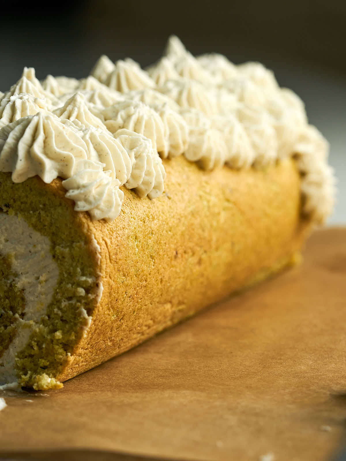 Side view of swiss roll cake topped with piped blobs of whipped cream.