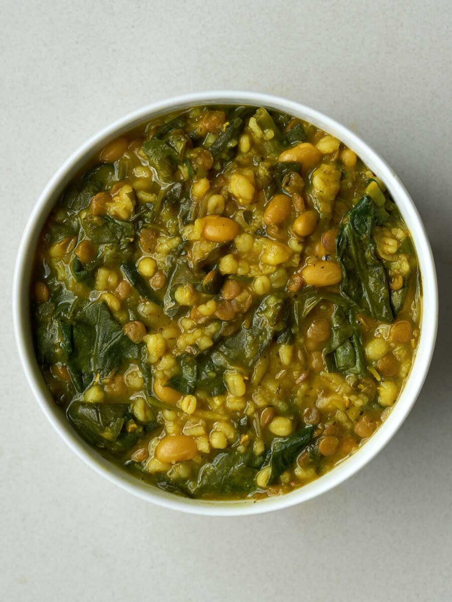 Top view of a bowl of mostly yellow and brown bean soup with cooked greens in it.