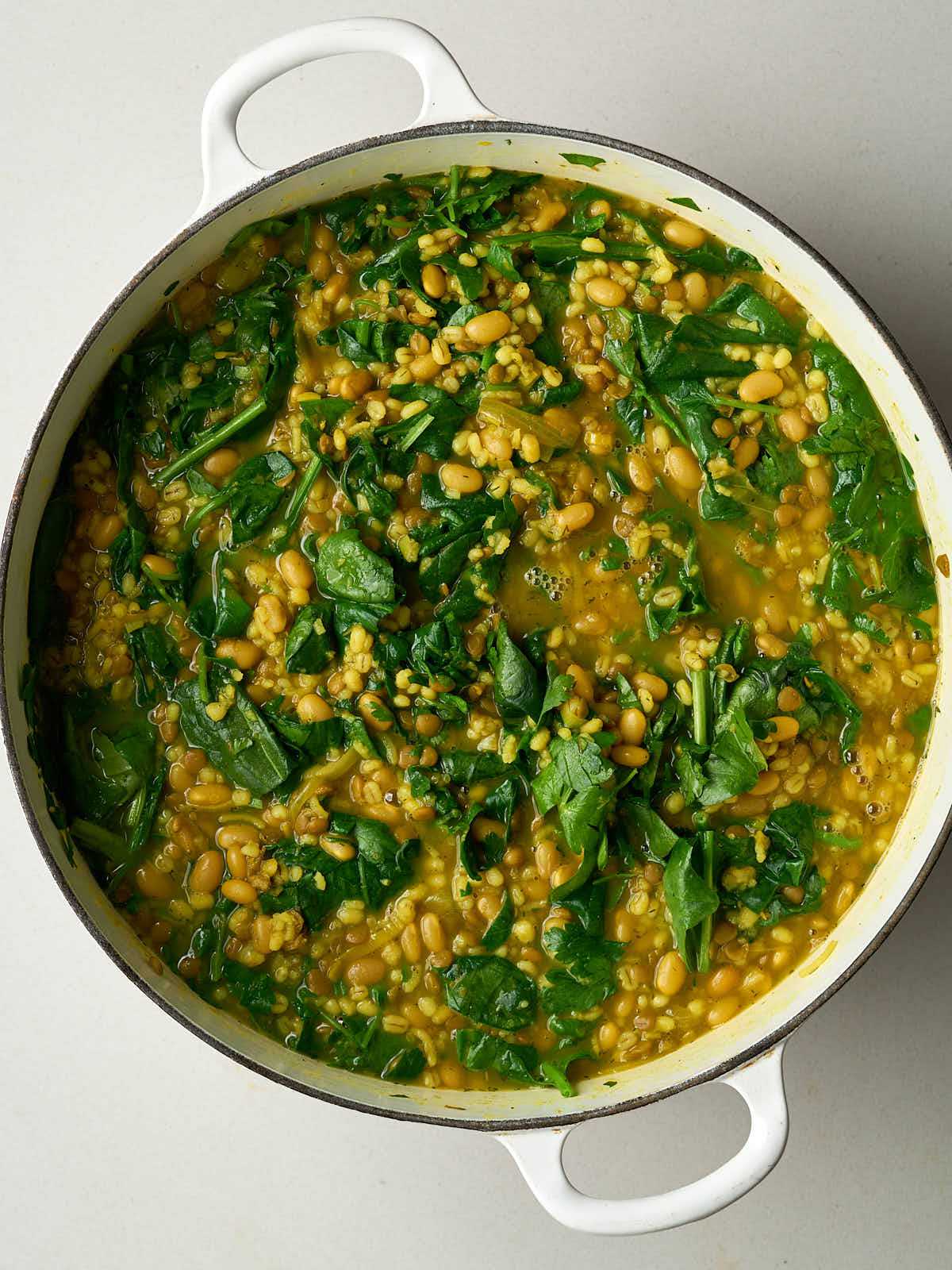 A large pot of yellow and brown bean soup with bright greens.