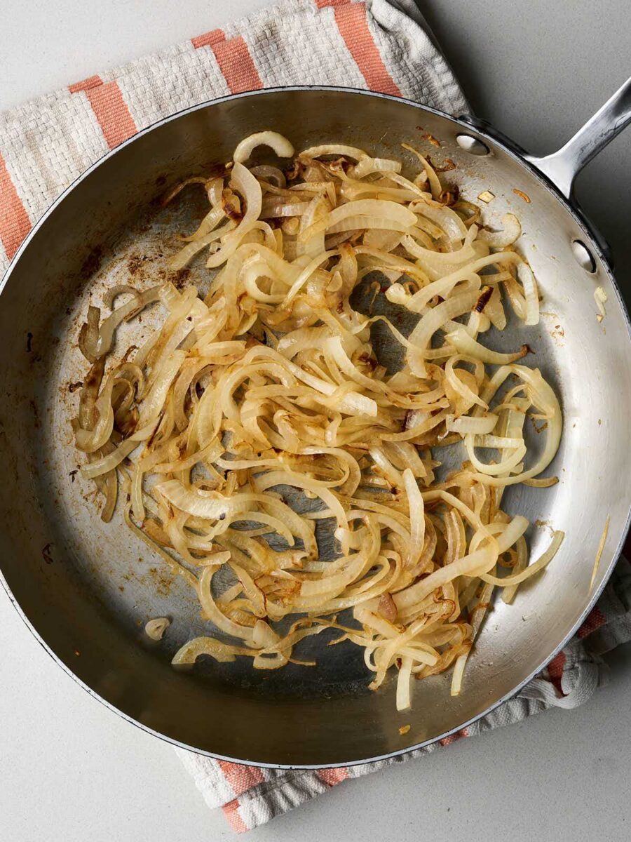 Lightly caramelized onion in a pan resting on a peach and white striped dish towel.