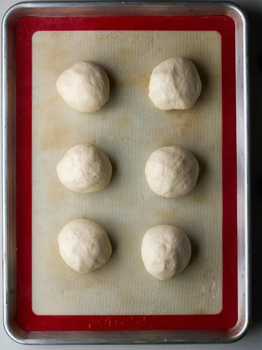 Balls of dough on a silicone baking mat lined sheet pan.