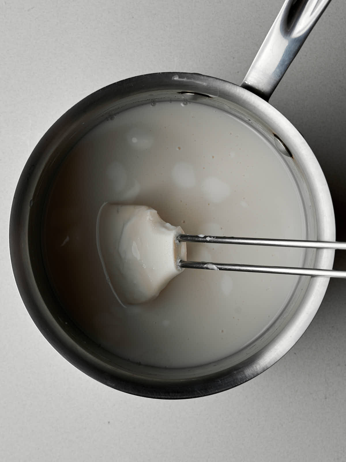 Coconut cream in a metal saucepan with a white silicone spatula.