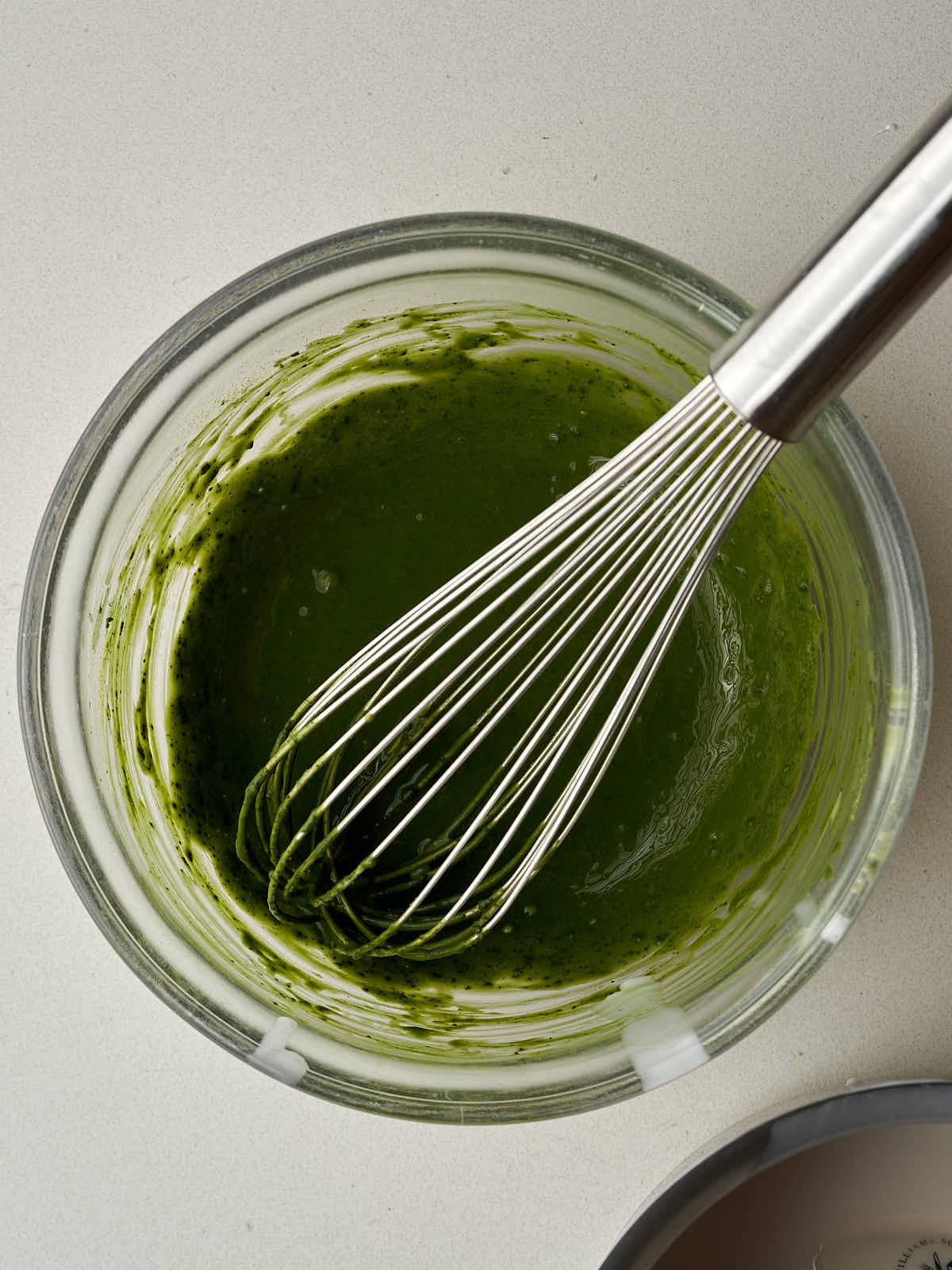 Green slurry in a glass bowl with a large metal whisk.