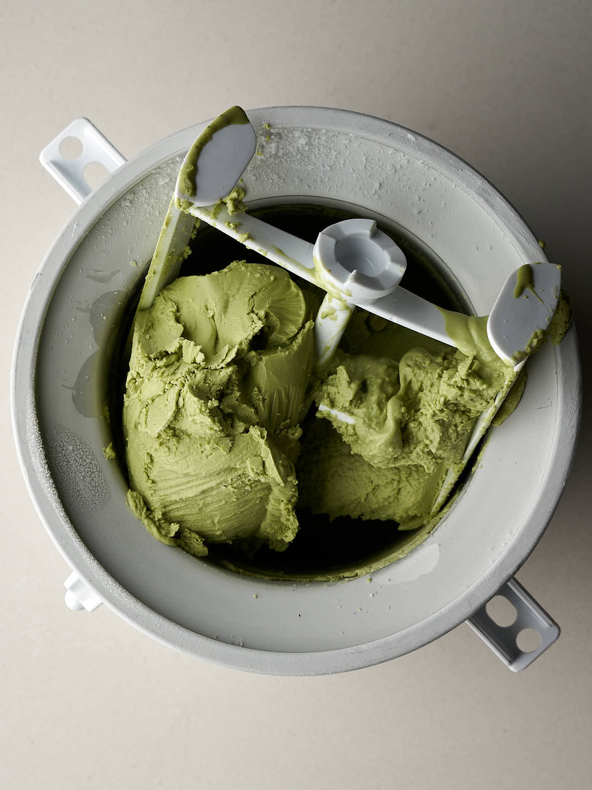 Stand mixer ice cream attachment with churned, green ice cream.