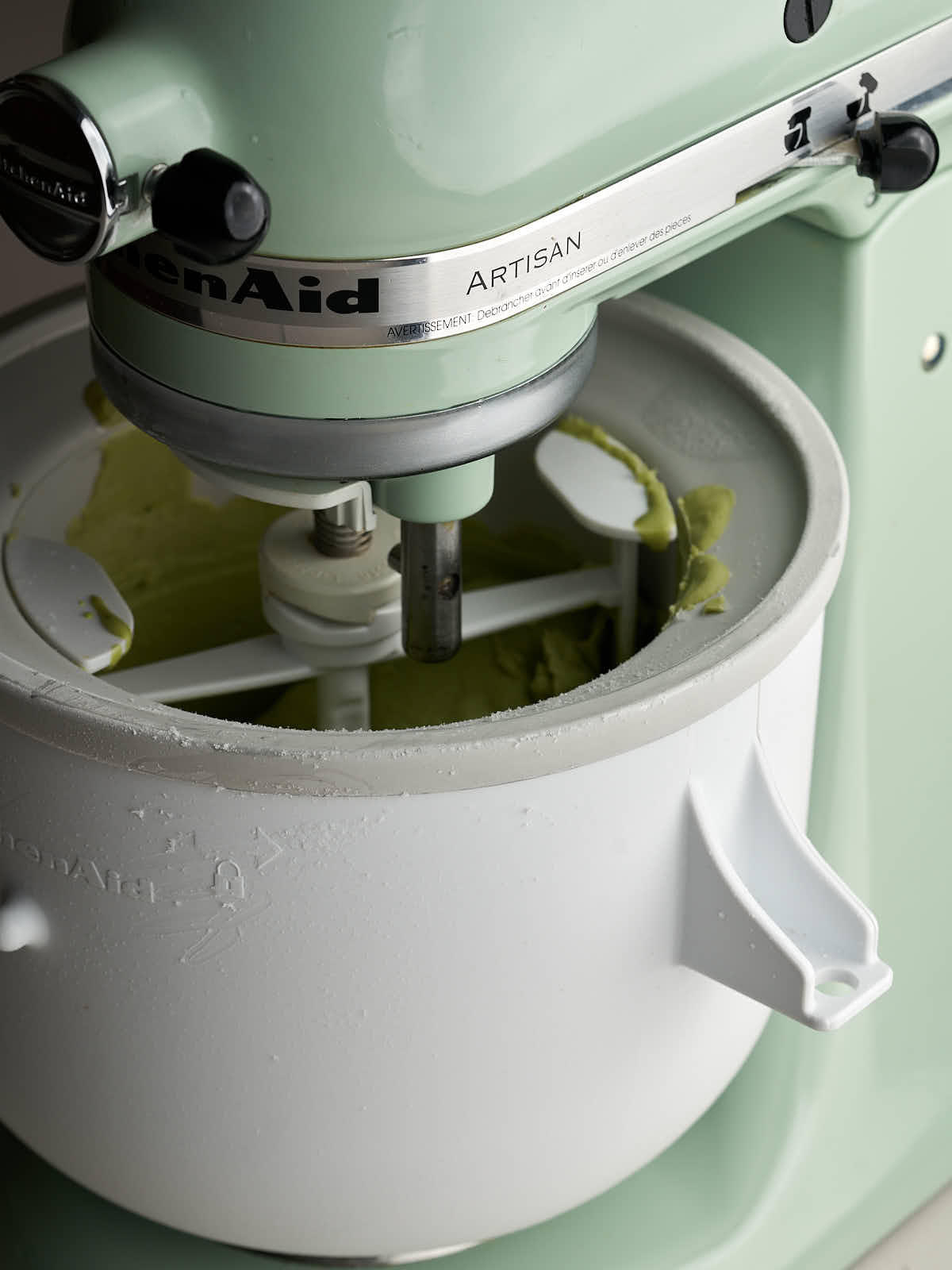 Green stand mixer with an ice cream attachment churning green ice cream.