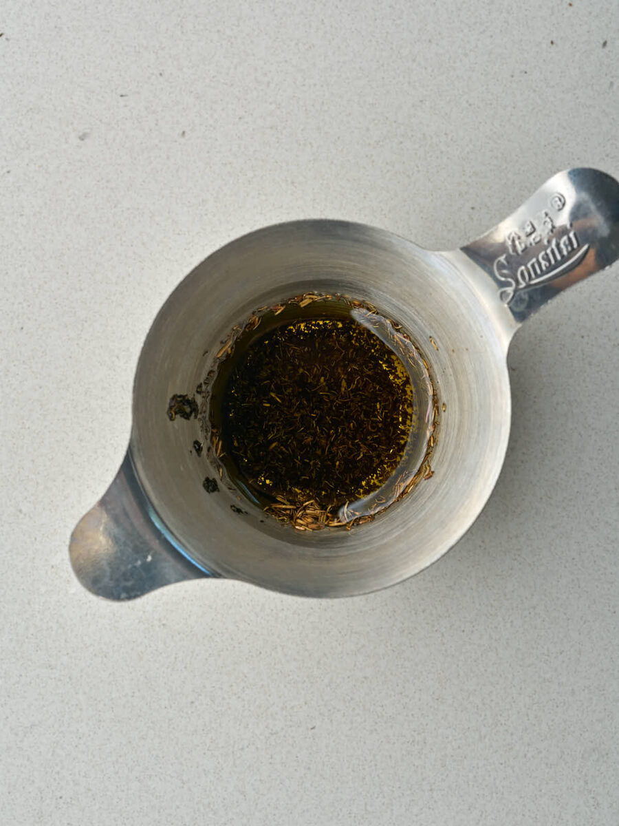 Metal strainer with olive oil and dried mint.