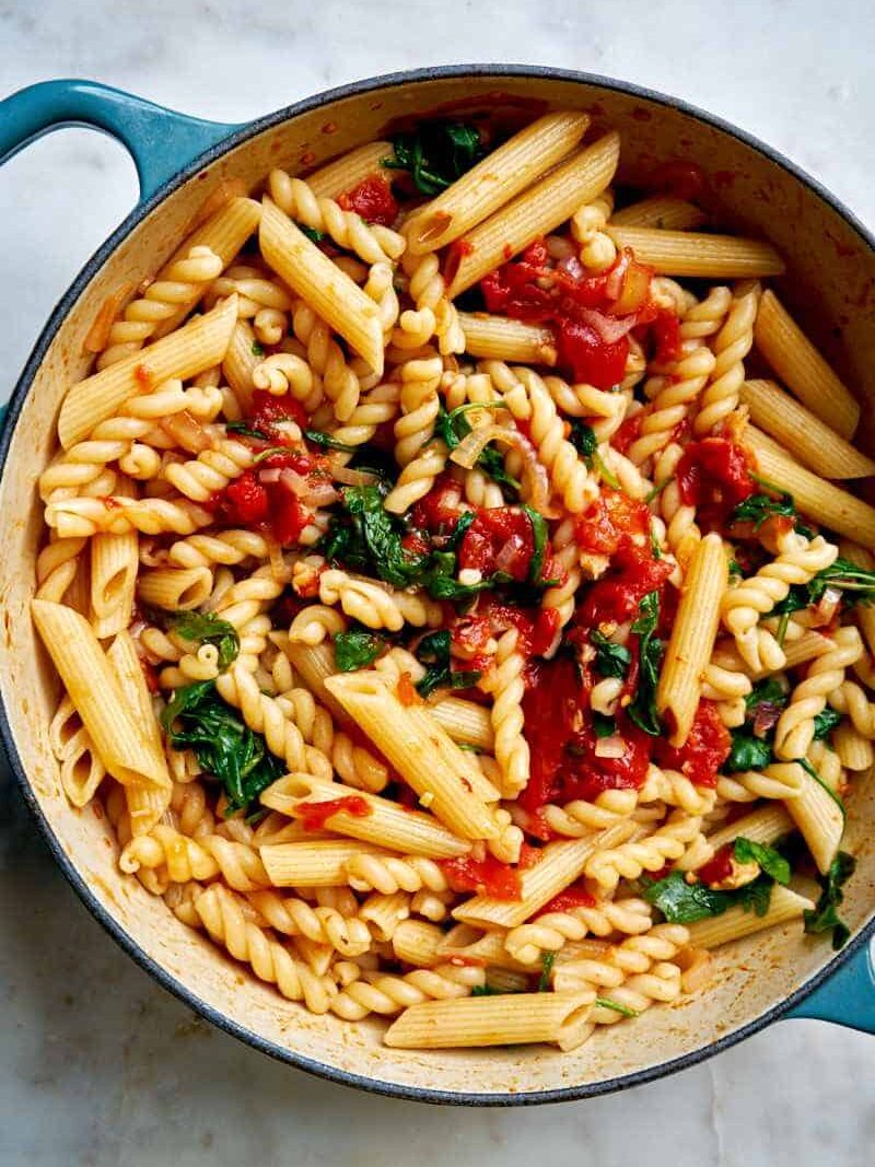 A large teal pot of pasta with tomatoes and arugula mixed in.