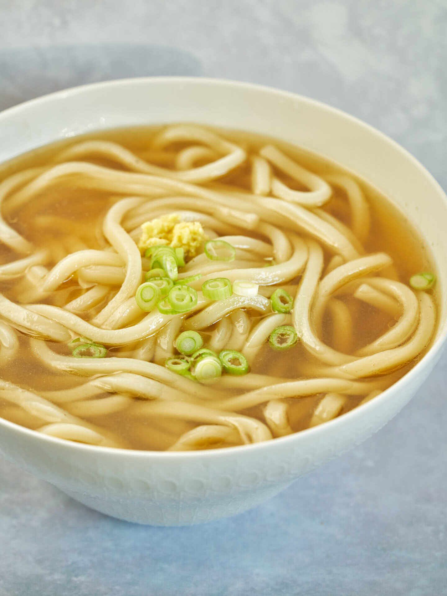 Side view of a white bowl with udon noodles and clear brown-toned soup.