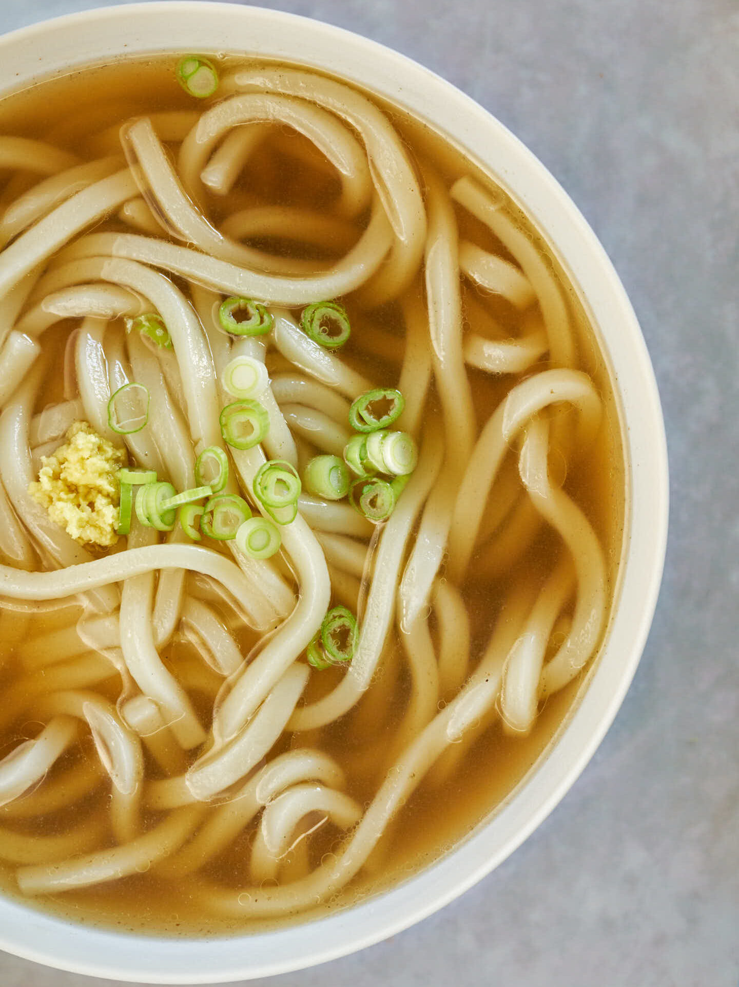 A white bowl with udon noodles and clear brown-toned soup.