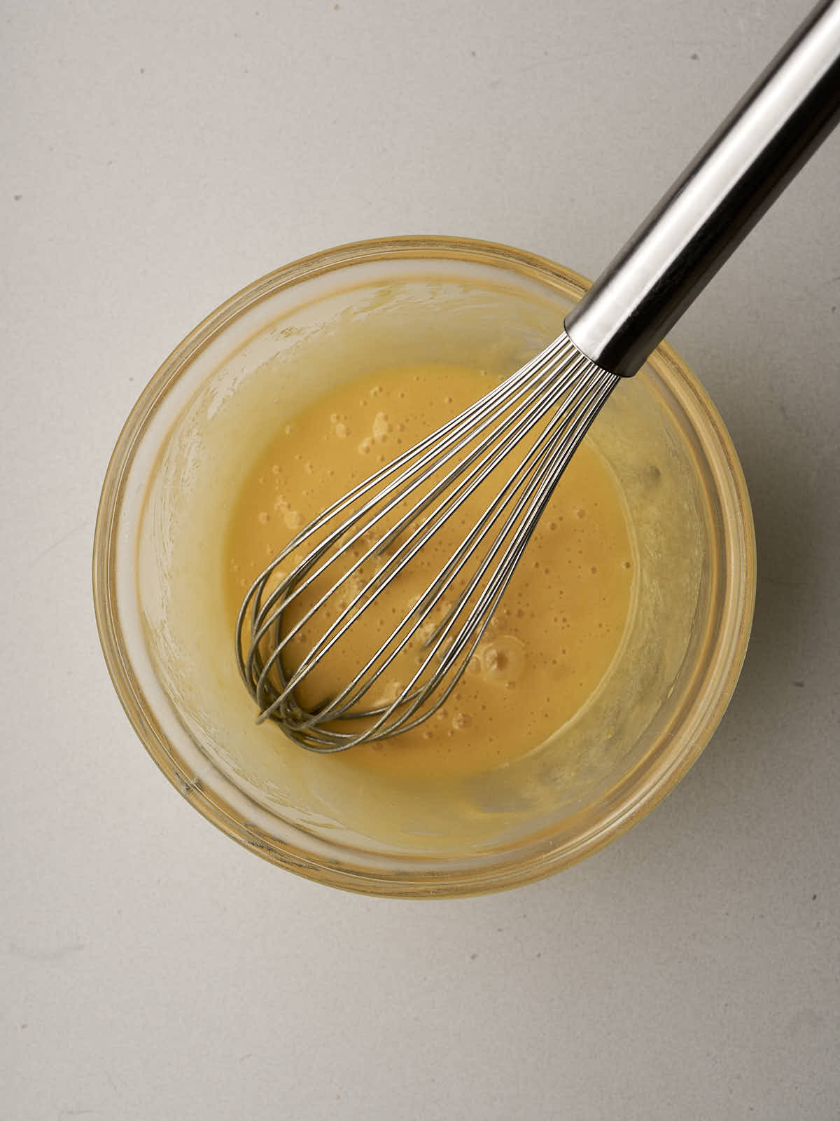 Pale yellow yolks in a glass bowl with a whisk.