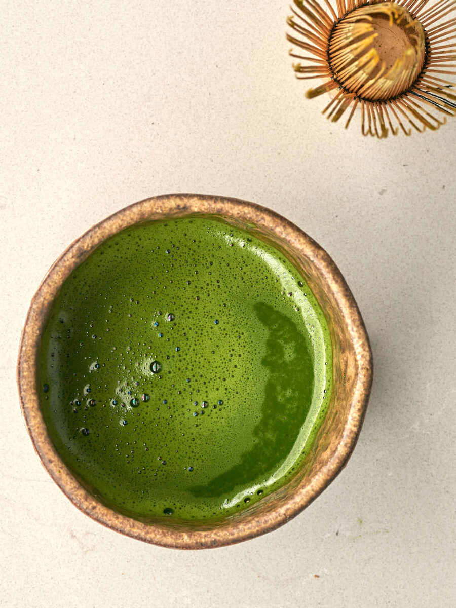 Bowl of matcha next to a matcha whisk.