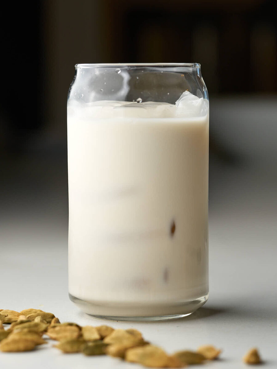 Glass of iced milk next to cardamom pods.