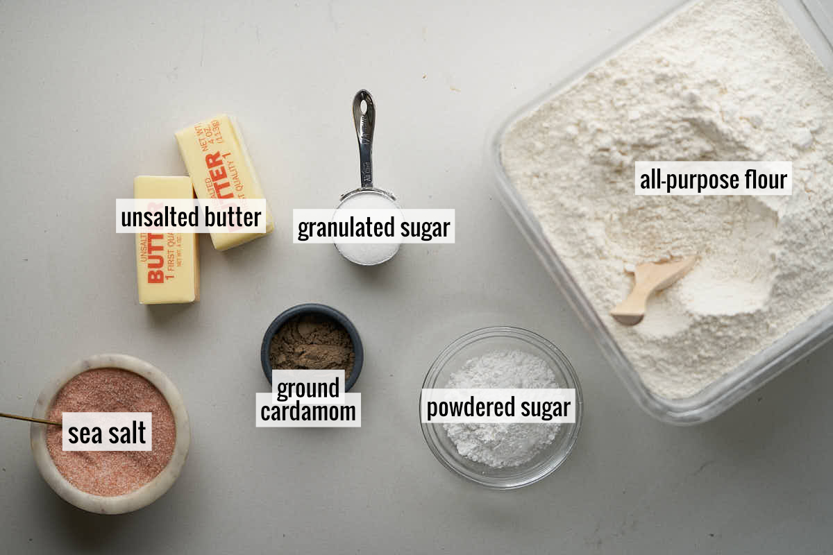 Ingredients to make shortbread cookies like flour, butter, and cardamom on a countertop.