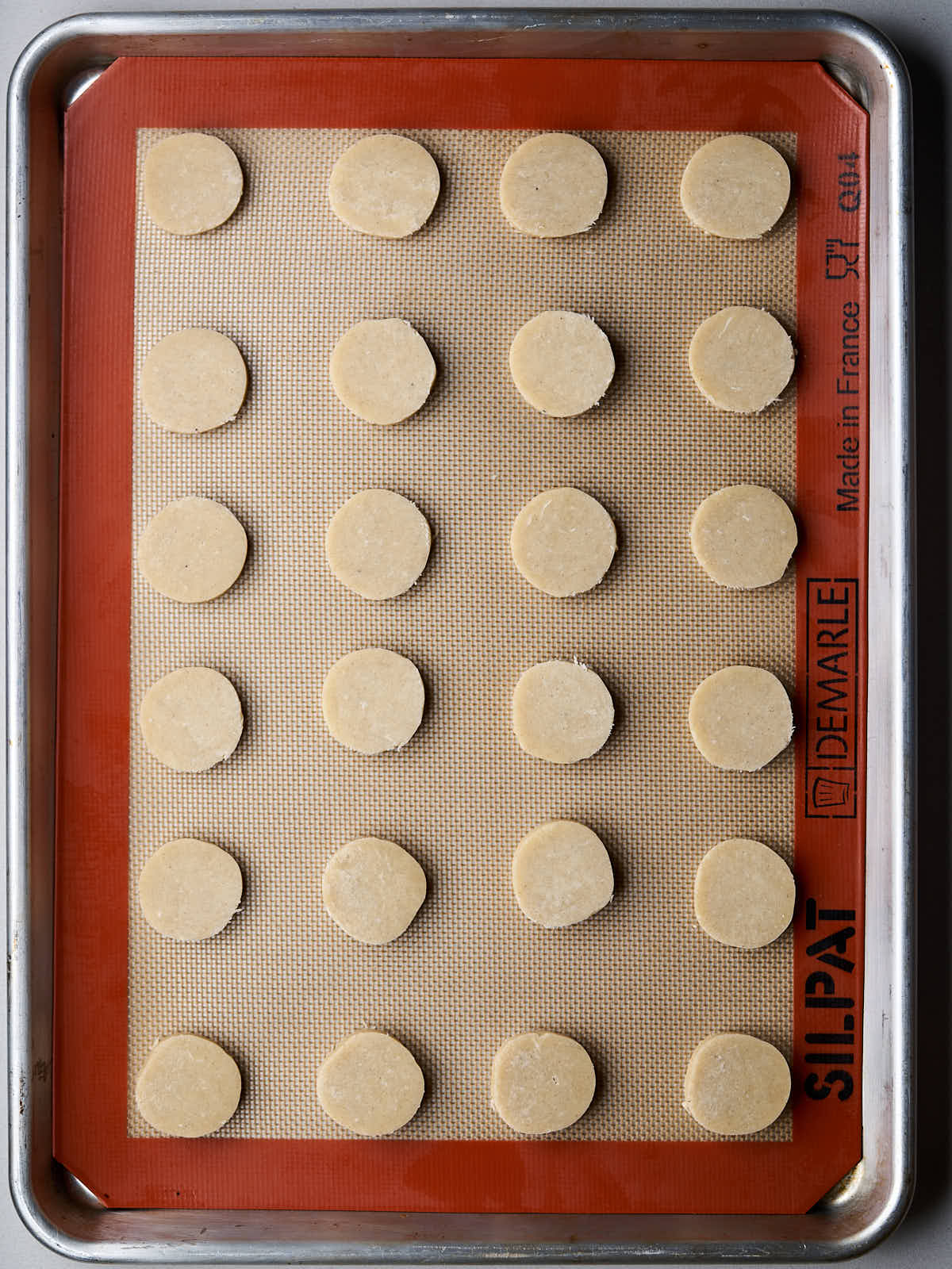 Six rows of four round shortbread cookies on a silicone mat lined baking sheet.