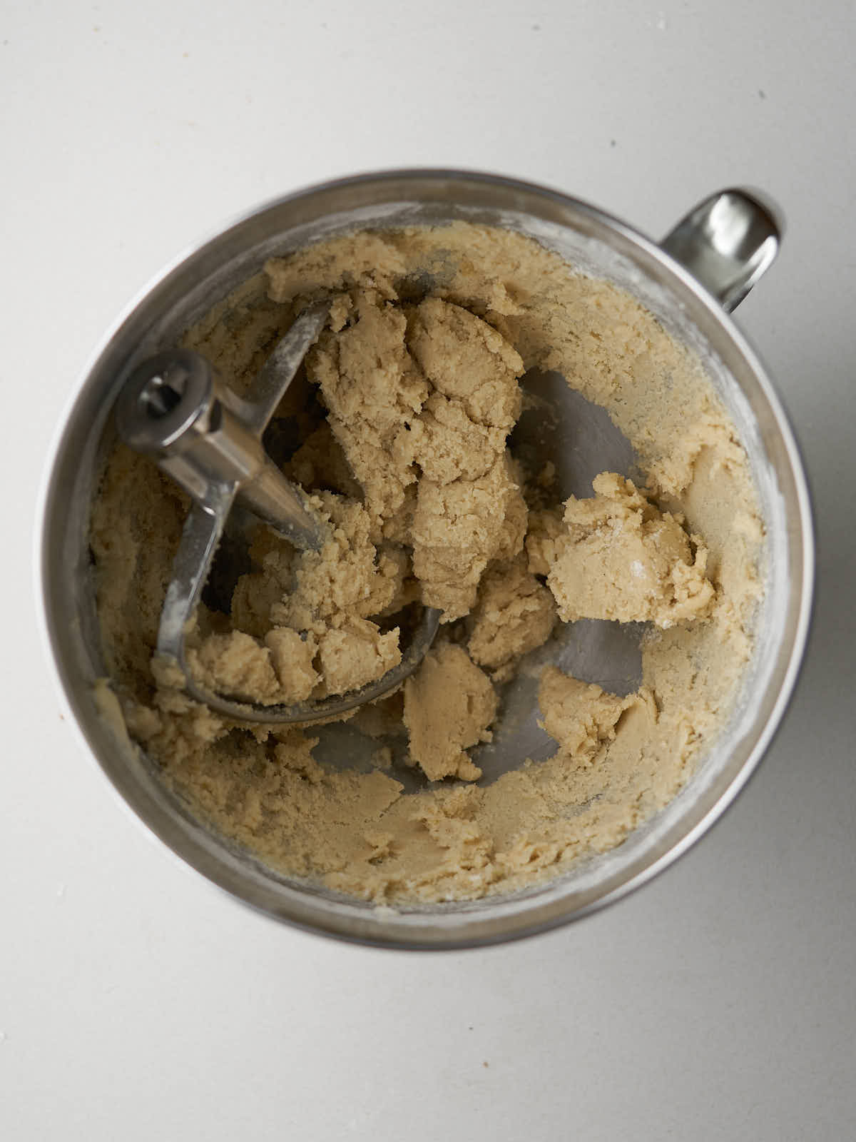 Cookie dough in the bowl of a metal stand mixer with a metal paddle attachment.