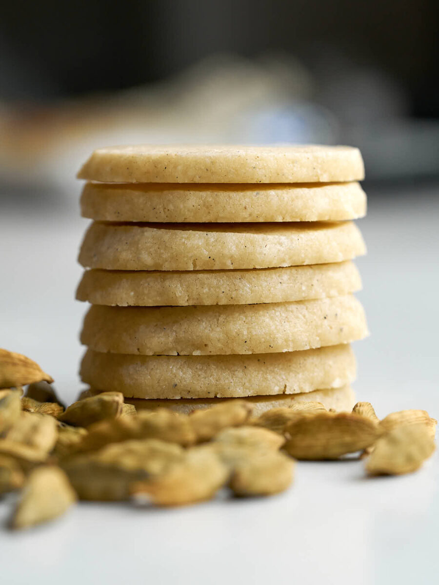 Stack of round shortbread cookies next to a pile of cardamom pods.