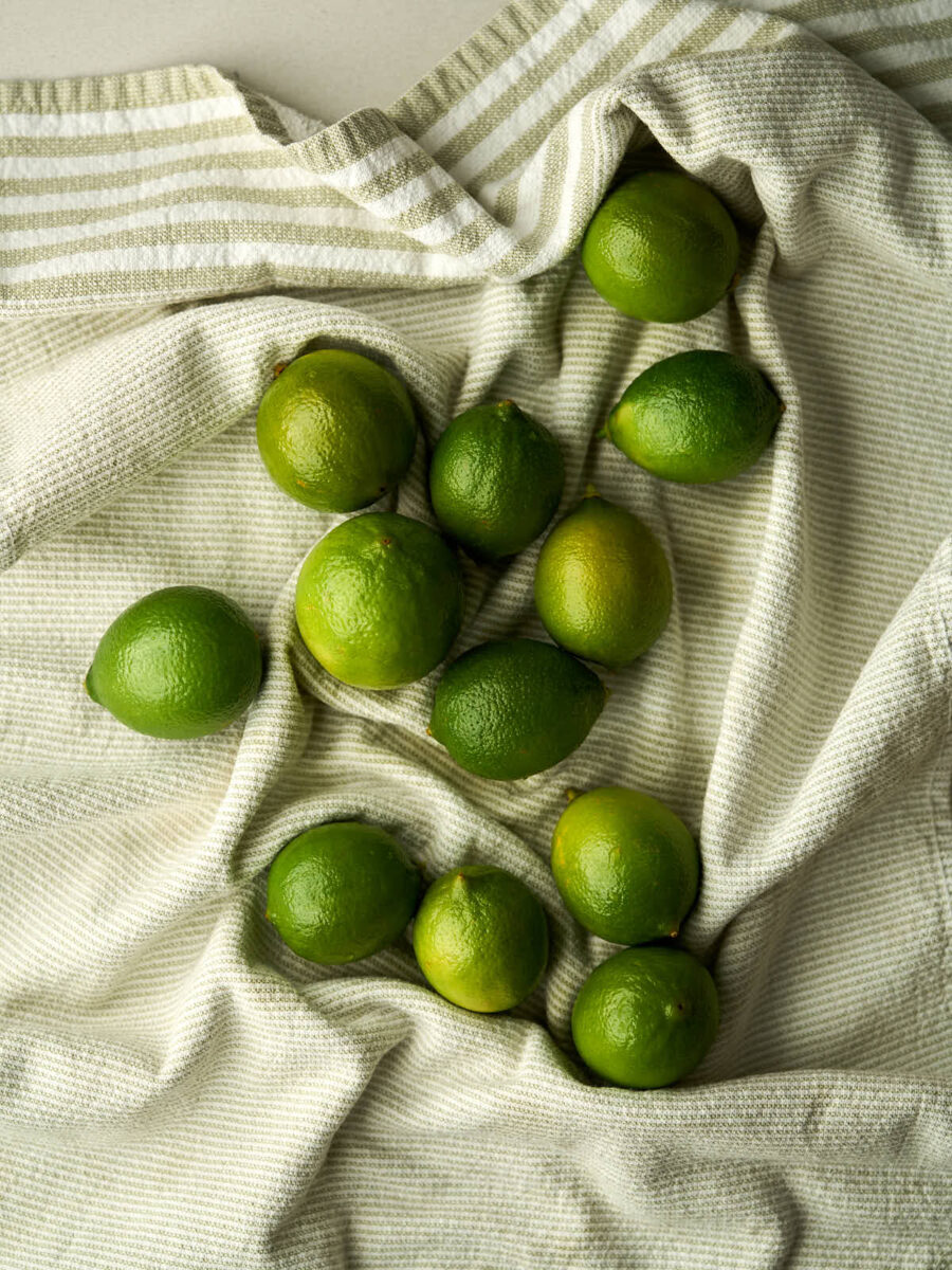 Twelve limes on a light green dish towel.