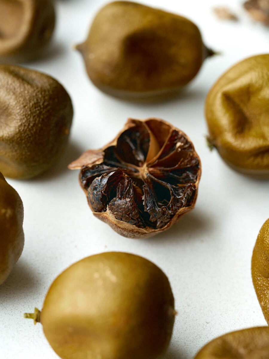 Dried limes on a countertop with the one in the middle cut open so you can see the dark brown flesh inside.