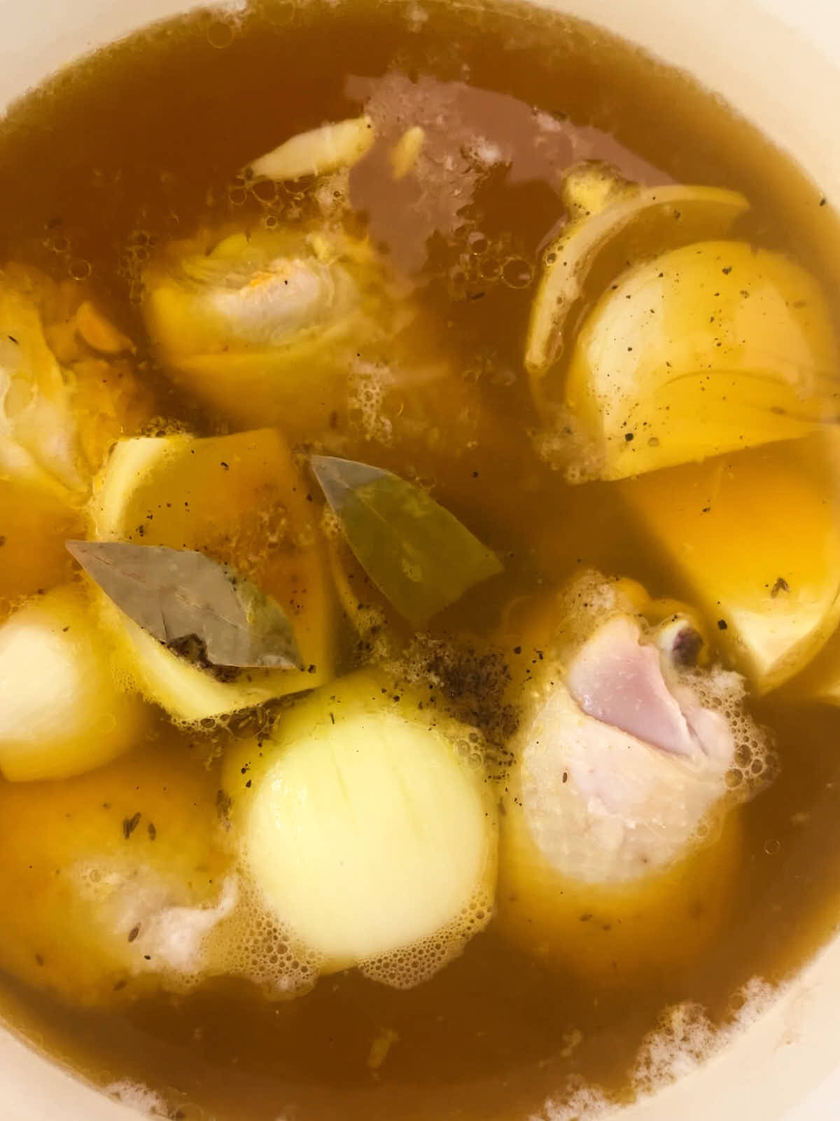 Chicken, onion, and a bay leaf simmering in a pot.