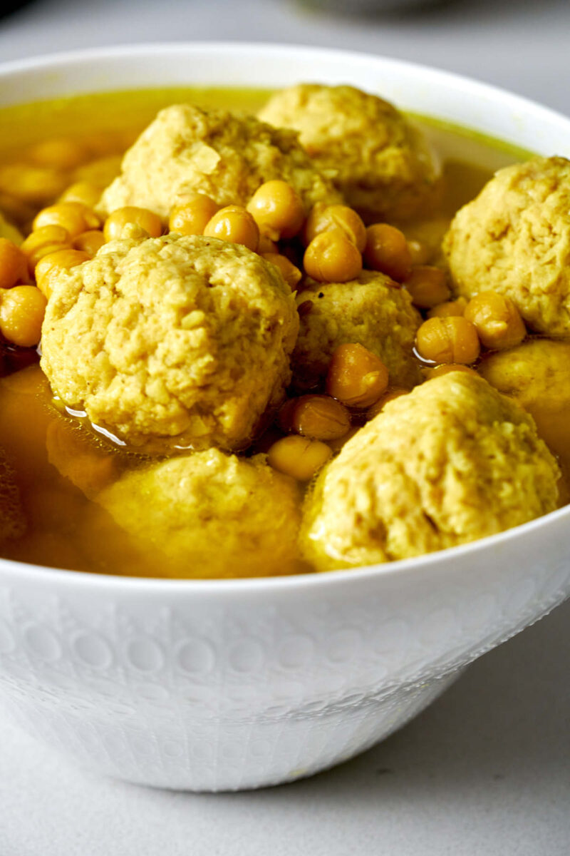 A white patterned bowl filled with chicken dumplings and chickpeas in a broth.