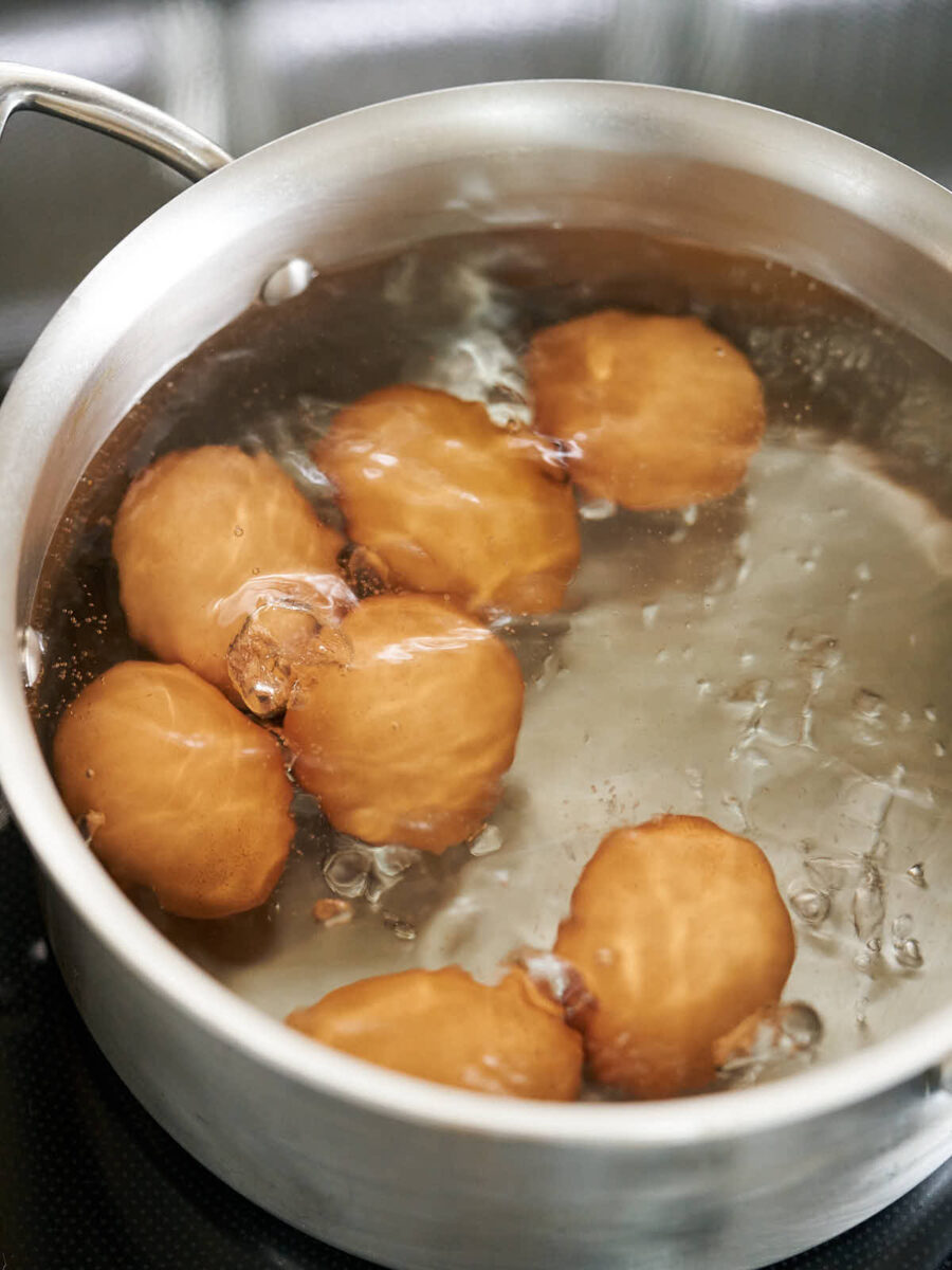 Brown eggs in a metal pot with boiling water.