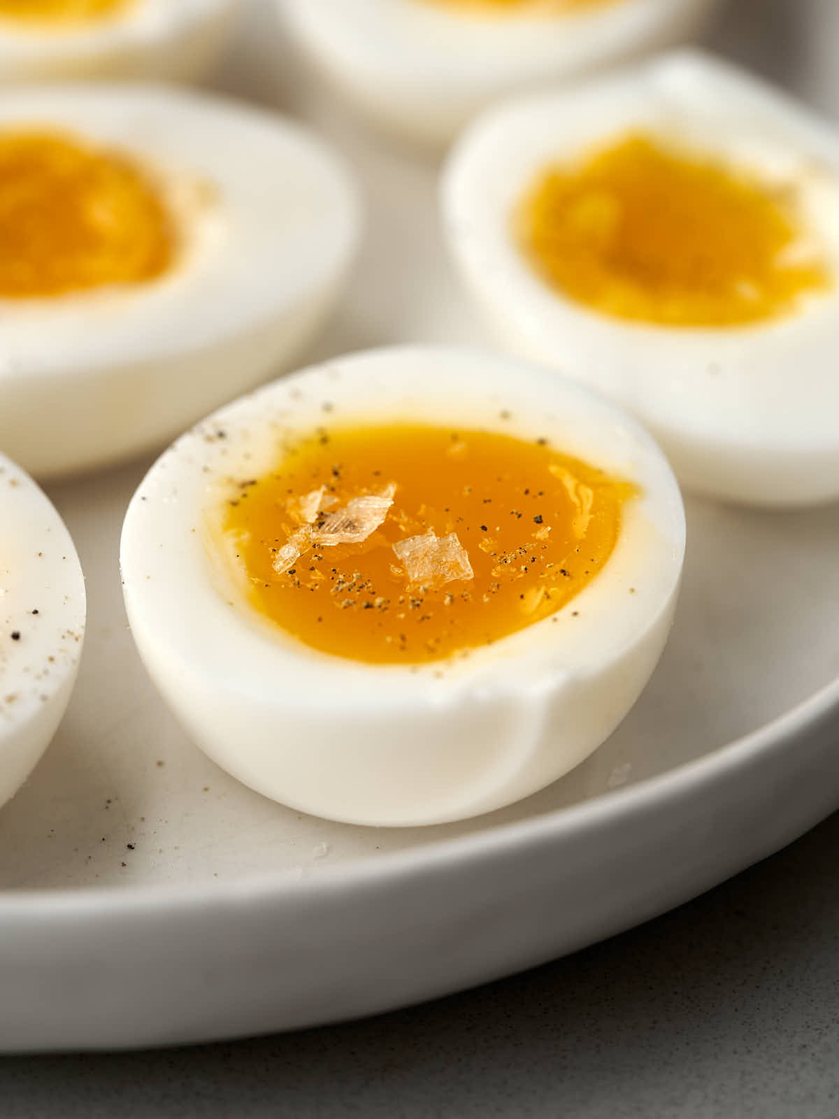 Jammy eggs on a white plate with flake salt and pepper.