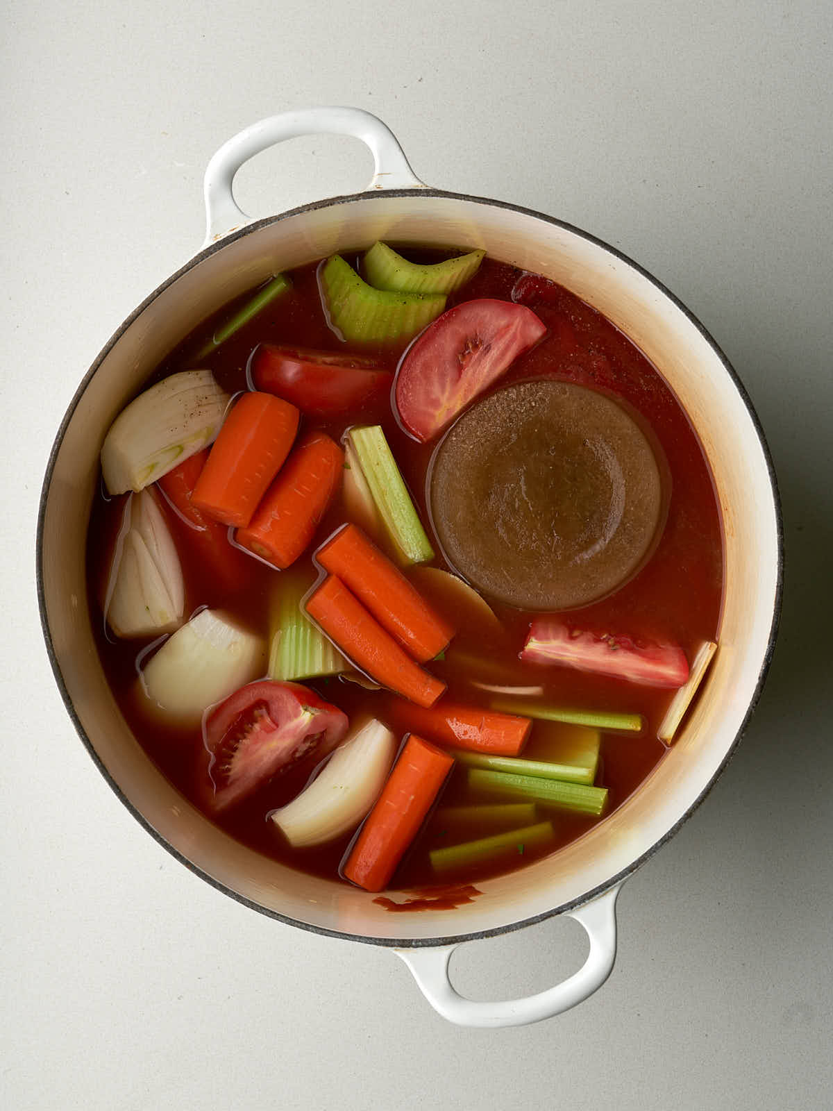 Carrots, celery, tomato and onion simmering in a red broth in a large pot.