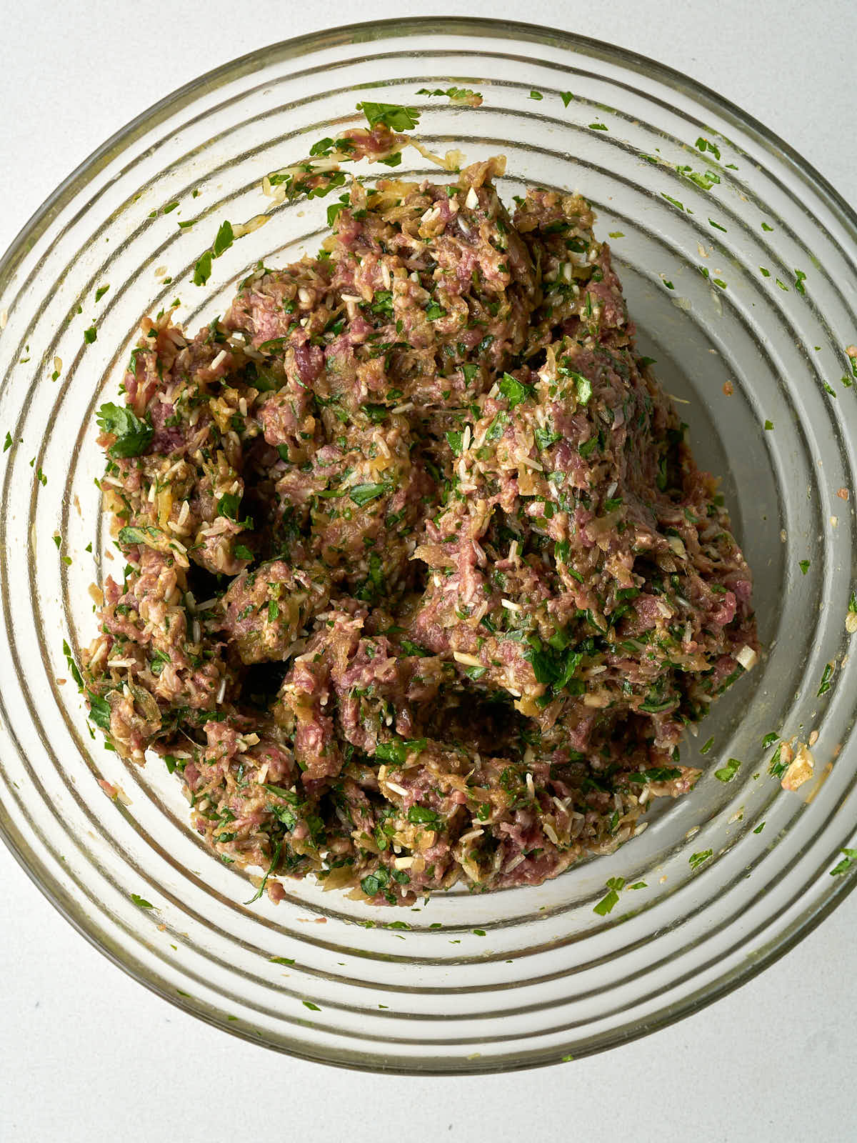 A raw meat mixture with rice and herbs in a large ribbed glass bowl.