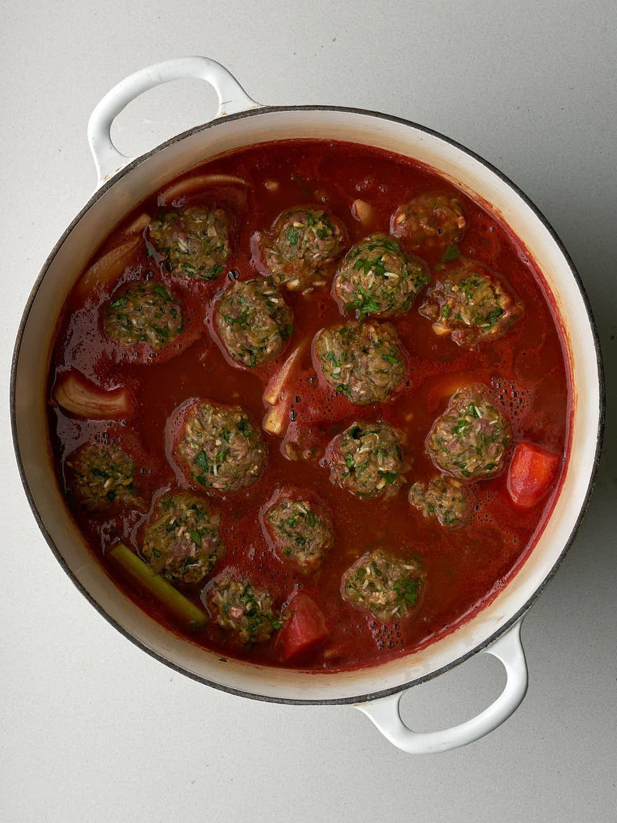 Meat and rice dumplings in a large pot of red sauce with vegetables.