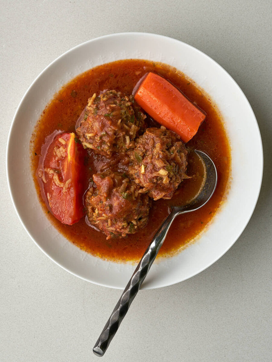 Three meatballs in a tomato broth in a small white bowl.