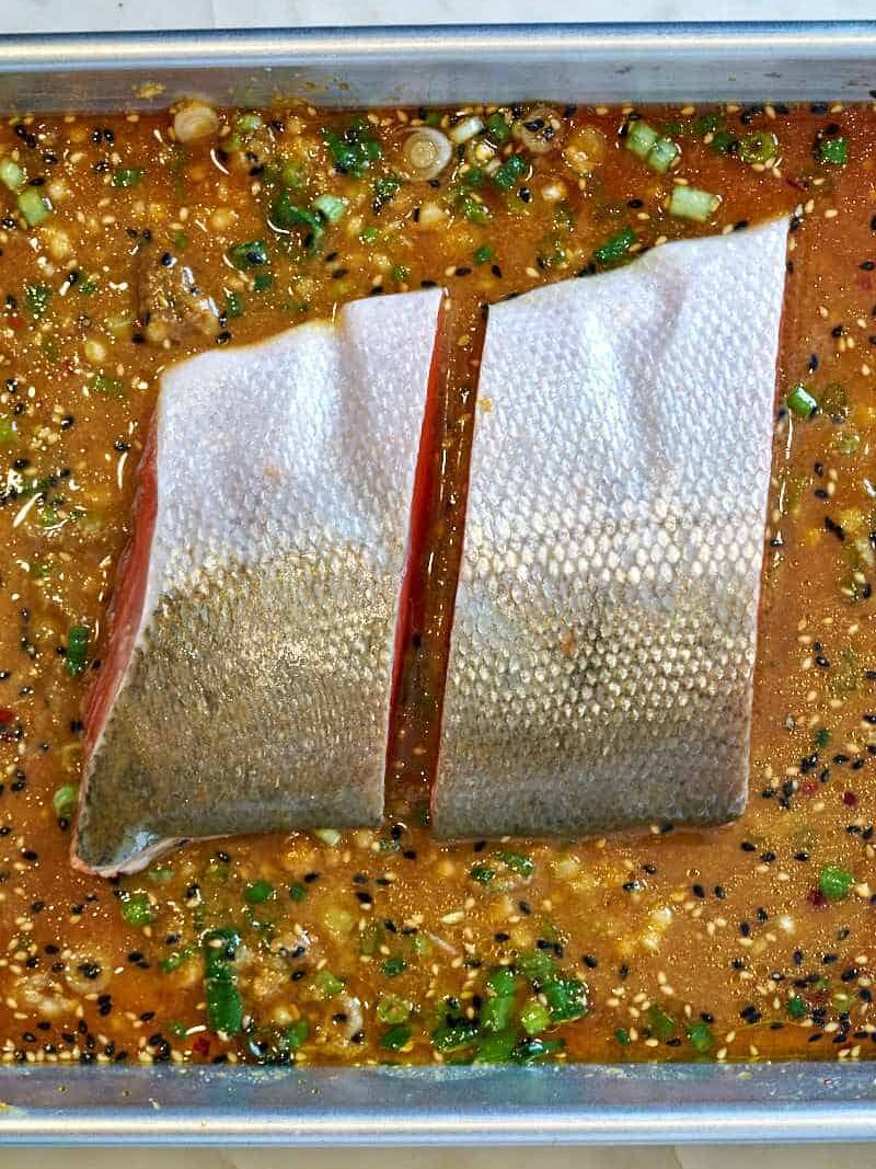 Two salmon filets face down on a baking sheet with a brown marinade.