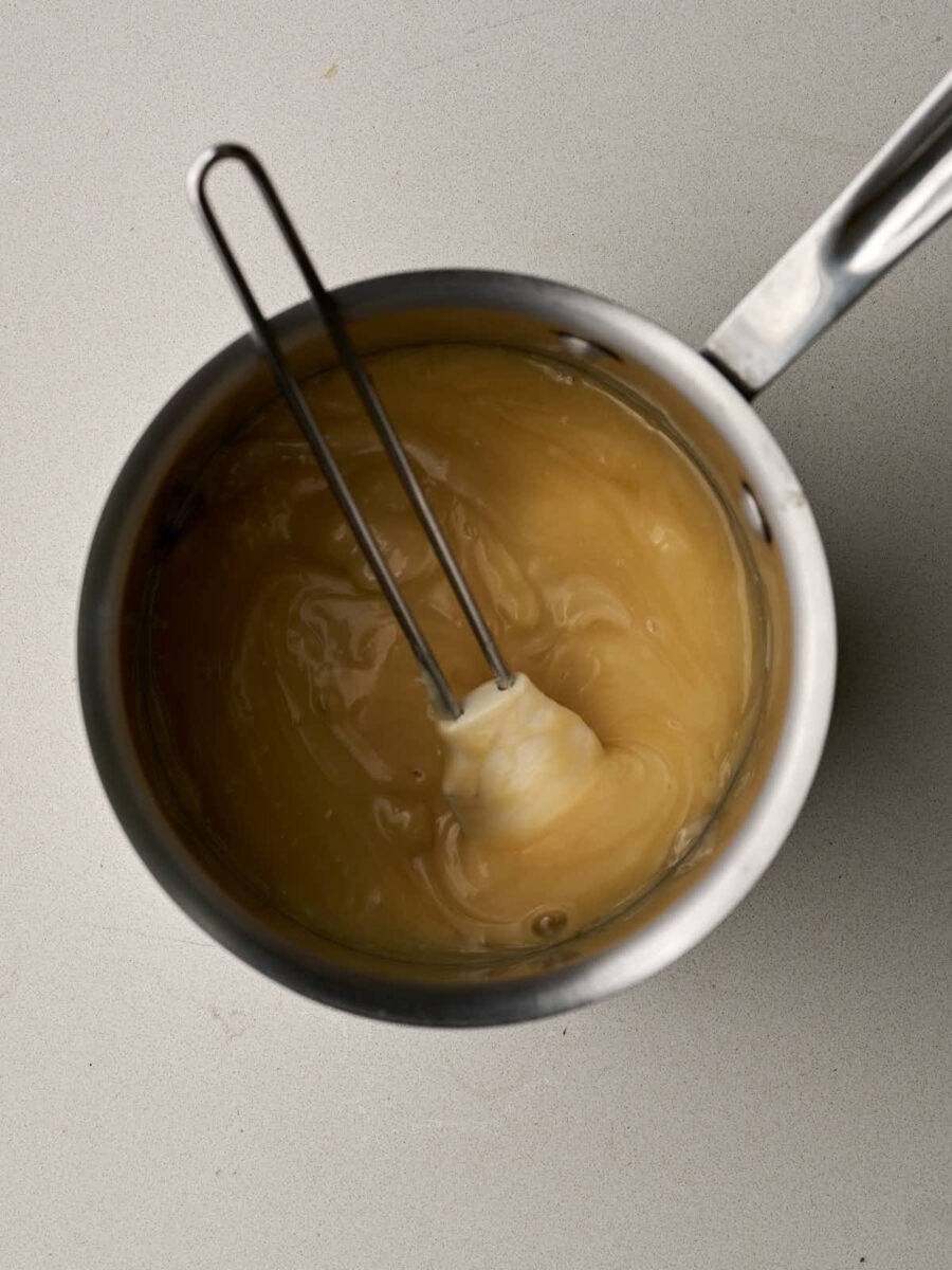 Sweetened condensed milk in a metal saucepan with a rubber spatula.