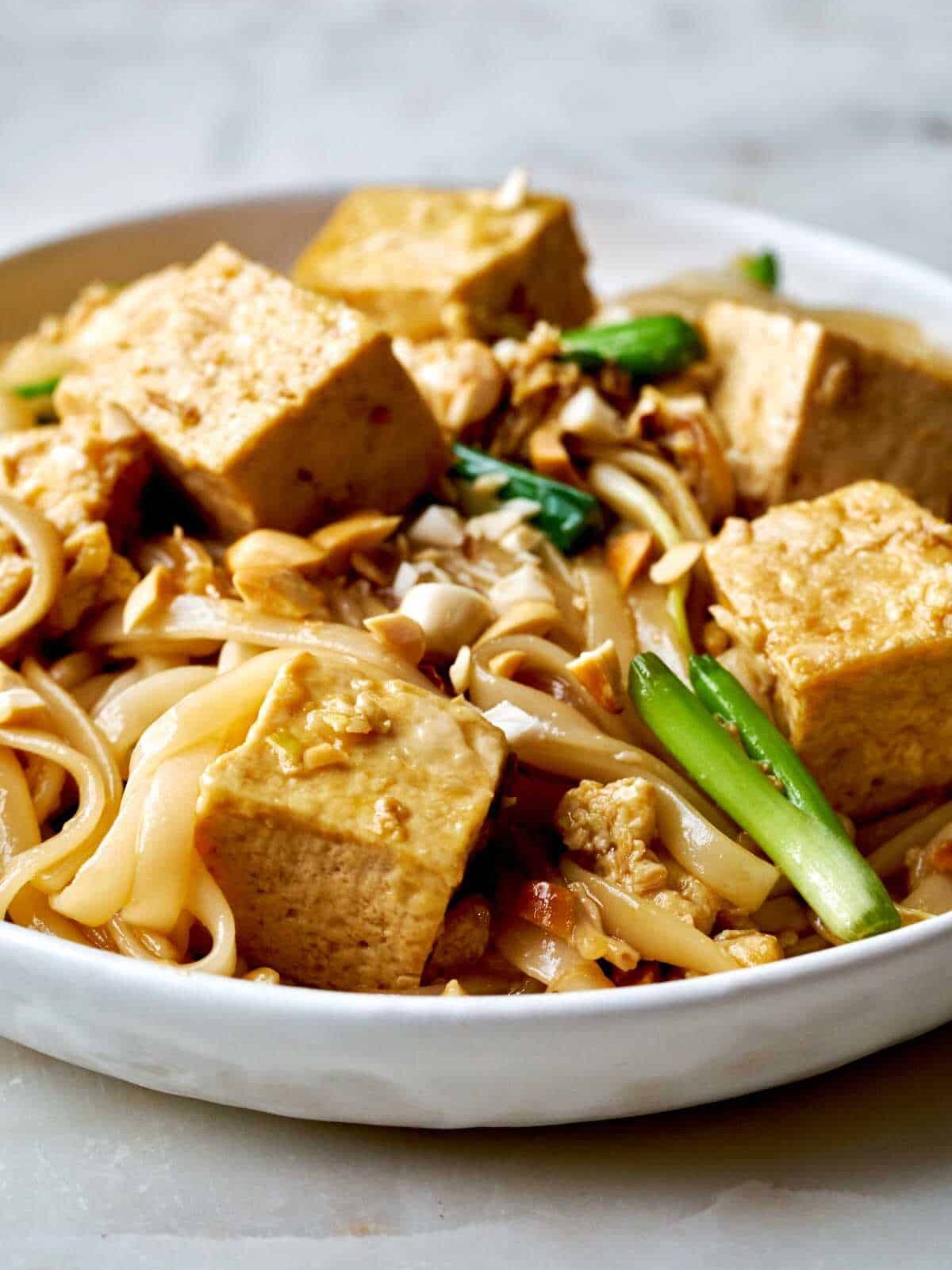 the side view of a tofu noodle stir fry on a white plate.