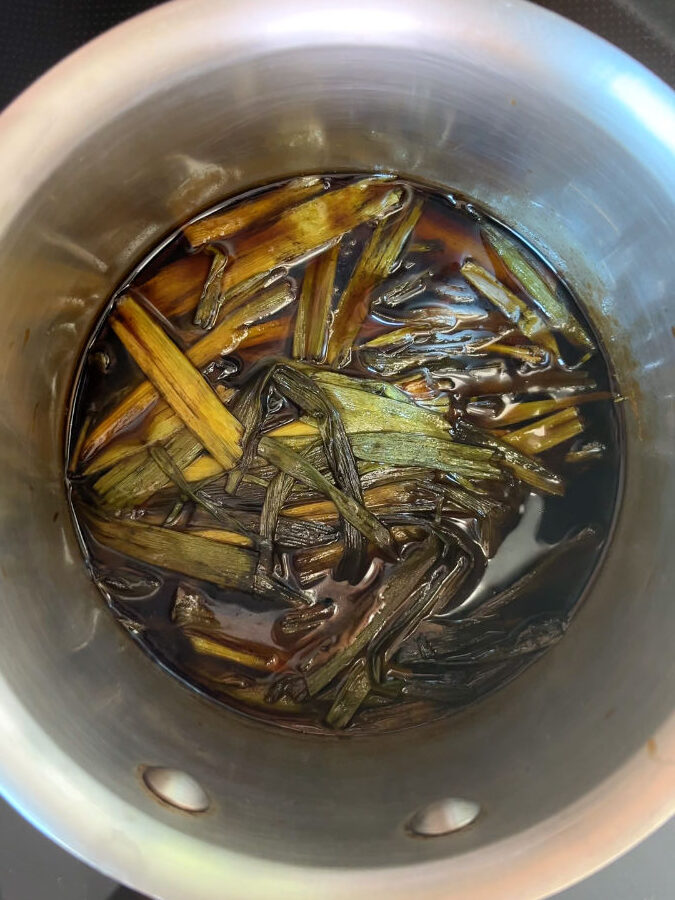 Dark brown sauce with cooked scallions in a large silver saucepan.