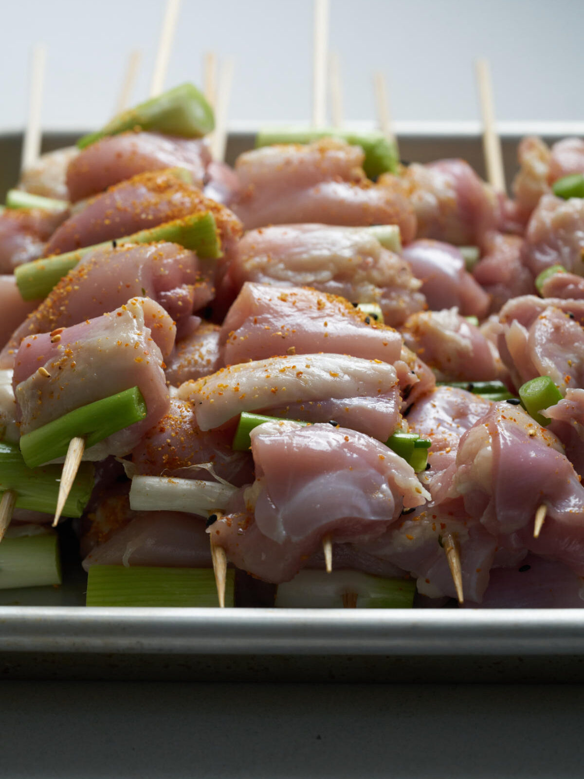 Stacks of raw chicken kabobs on skewers with scallions and spices.